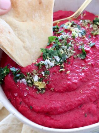 beet hummus in bowl with piece of pita bread dipped into the hummus