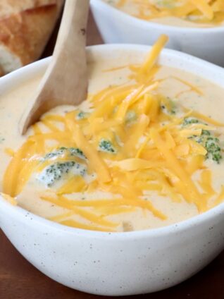 broccoli cheddar soup in bowl topped with shredded cheddar cheese with wooden spoon in the bowl
