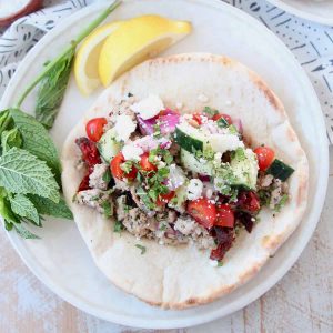 Greek gyro in pita bread on plate with lemon wedges and fresh mint
